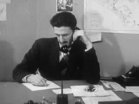 A man sitting at an office desk talking on the telephone.