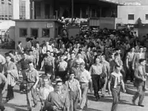 Crowd of men in work clothes walking outside industrial facility