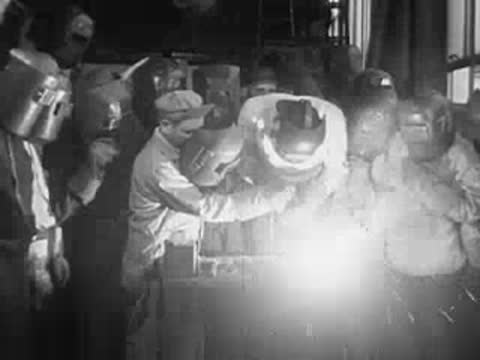 Workers performing welding work with bright sparks in a workshop.