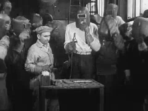 Group of workers observing a welding demonstration around a table.