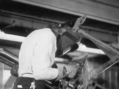 A welder in protective gear operating machinery under industrial beams.