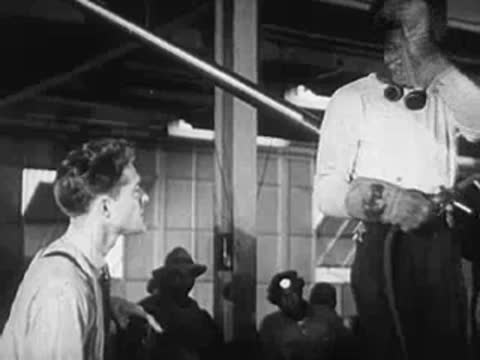 A man talking to a worker holding up a welding mask in a factory.