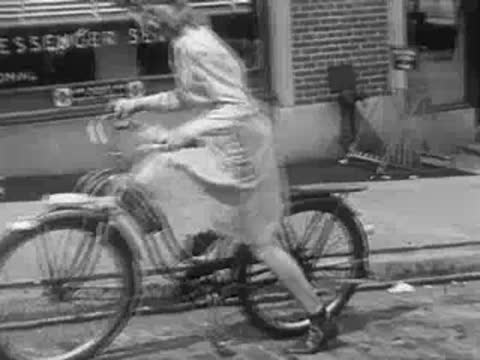 A woman riding a bicycle past a messenger service building.
