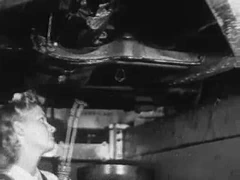 A mechanic looking up and operating equipment underneath a car lift.