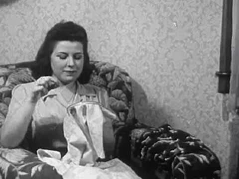 A woman sitting in an armchair stitching fabric with embroidery hoops.