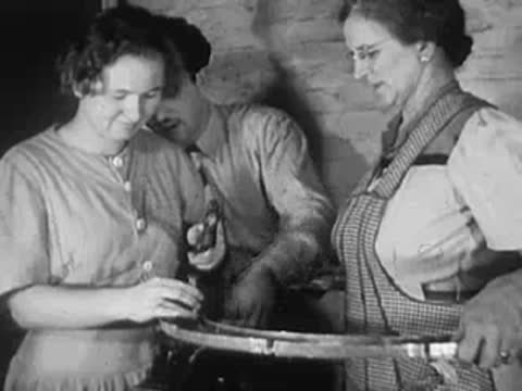 Two women and a man working with circular metal parts in a workshop.