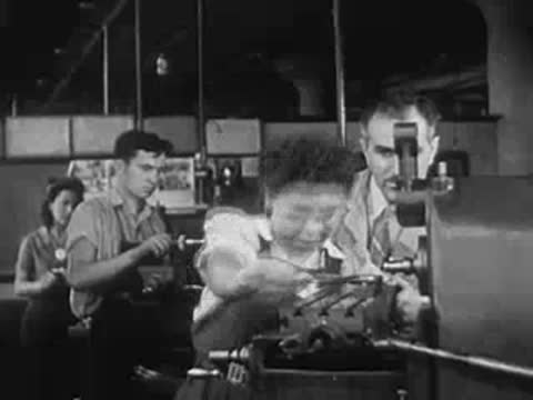 A woman operating a machine with male coworkers supervising in a factory.