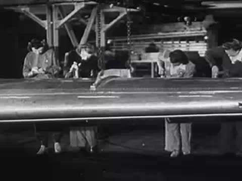 Line of workers performing detailed assembly work on a large metal structure.
