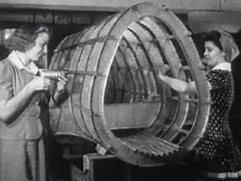 Two women using power tools to assemble a large curved metal frame.