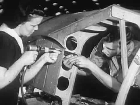 Two workers using power drills to assemble metal aircraft framework.