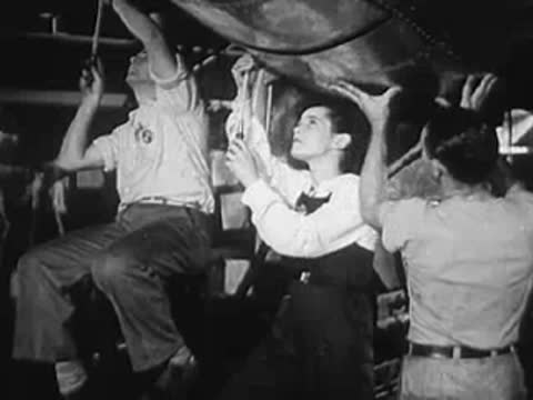 Workers assembling metal framework inside a factory with a pay line sign.
