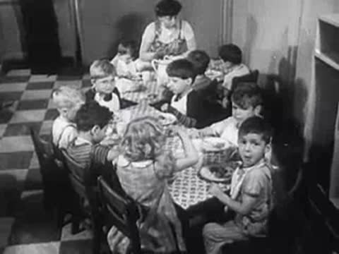 Children sitting around a table eating a meal while adults supervise