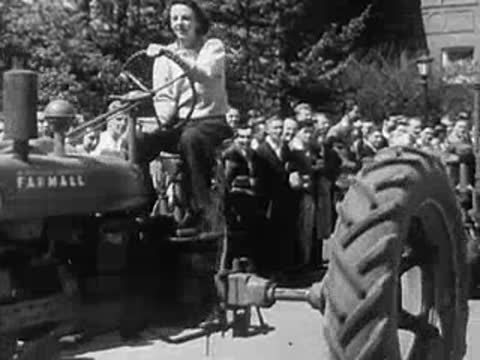 Woman smiling while driving a tractor with a crowd watching