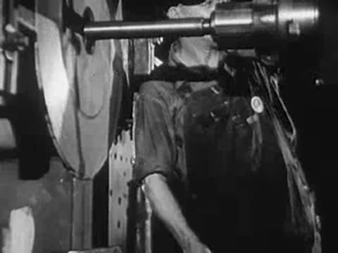 Factory worker operating a large lathe machine, protective cap