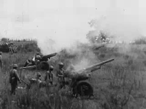 Soldiers in uniform loading and firing a field artillery gun outdoors