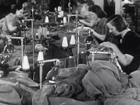 Several women working at industrial sewing machines in a large manufacturing or garment factory.