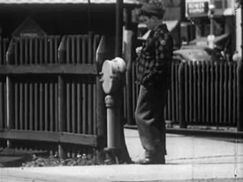 Boy walking along a sidewalk near a wooden fence and brick building.