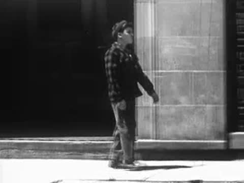 Boy walking along a city sidewalk past a building entrance.