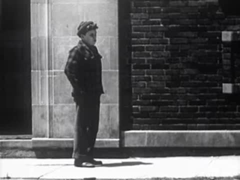 Boy standing on a city sidewalk next to a brick building facade.