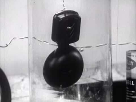 Close-up of a ringing bell suspended inside a glass jar in a laboratory.