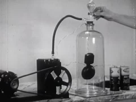 Scientist operating a vacuum pump valve next to a glass bell jar.