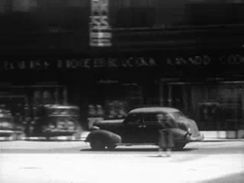 Car driving past Sears Roebuck and Co store on a city street.