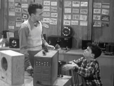 Instructor talking to boy sitting at laboratory desk with equipment