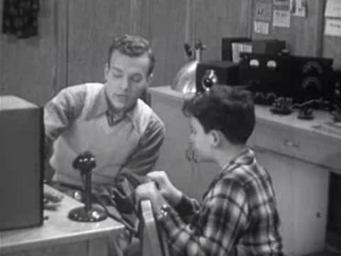 adult teaching a boy in a room with vintage electronic equipment