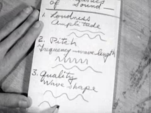 hands writing science notes including wave shape in notebook