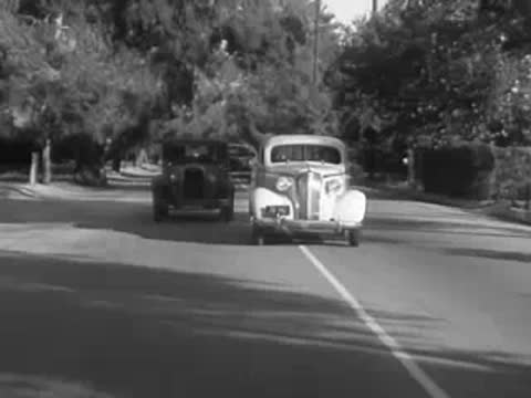 A vintage car driving behind another vehicle on a road.