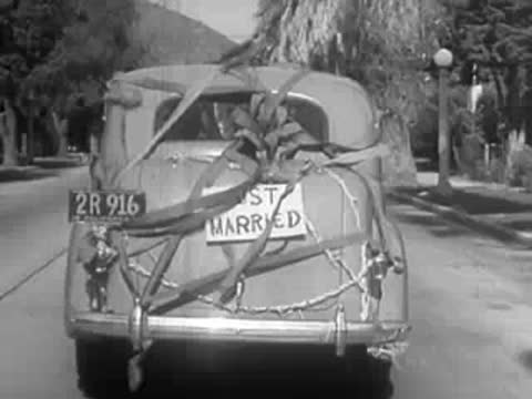 Rear view of a vintage car with "Just Married" sign and branches attached.