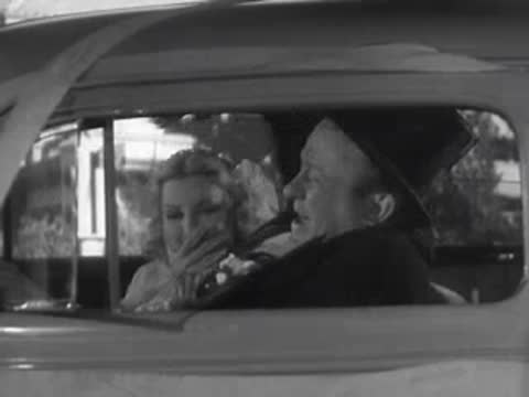 A smiling couple sits together inside a vintage car in 1937.