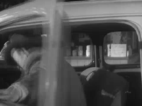 A man wearing a hat gets into the driver seat of a vintage car.