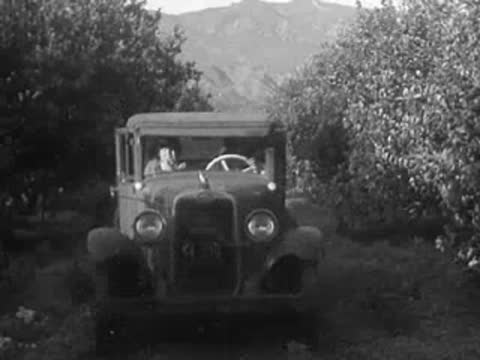 A vintage car driving down a dirt road through trees.