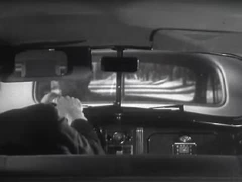 View from inside a car showing the road reflected in the rear-view mirror.