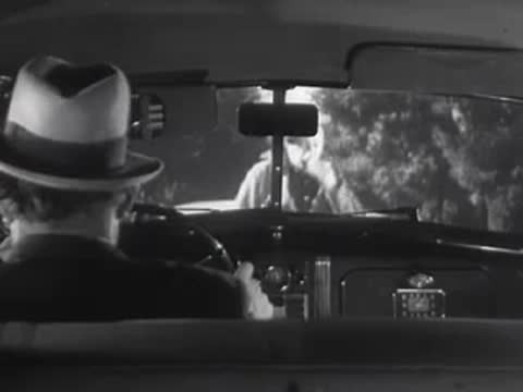 A driver looks back as another person approaches the car.