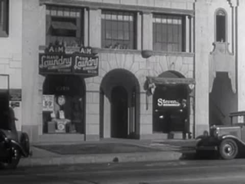 A black car drives past a building with laundry and store signs.