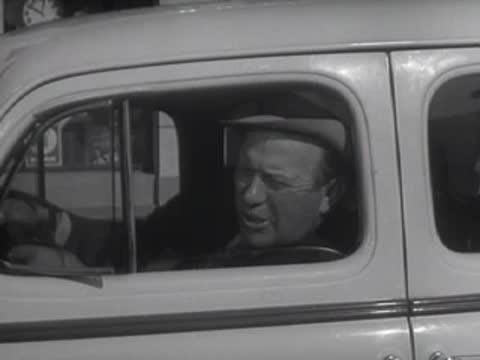 A driver looks out the window of a car on a city street.