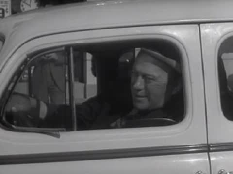 A driver sits inside a parked car in front of a commercial building.