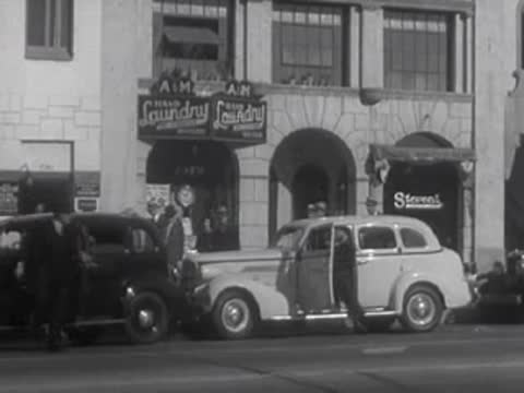 A person exits a black car parked next to a white sedan on a street.