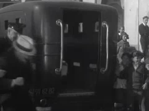 People gather around the rear doors of a dark van on a city street.