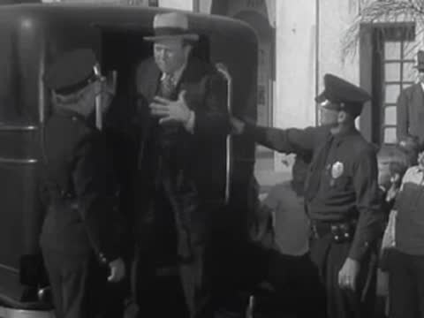 A man is escorted by police officers into the back of a van.