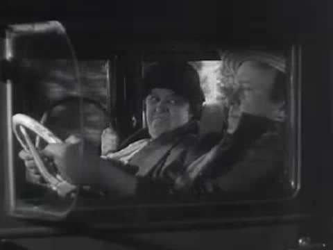 Driver and passenger inside a vintage car looking ahead.
