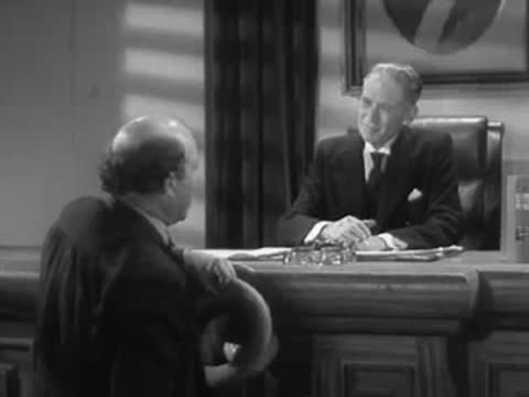 Two men shake hands across an office desk under the watchful eye of an official.