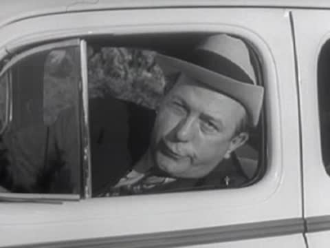 Driver gestures and hides face inside a vintage automobile.