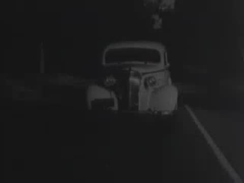 Vintage car driving forward on a sunny tree-lined road.