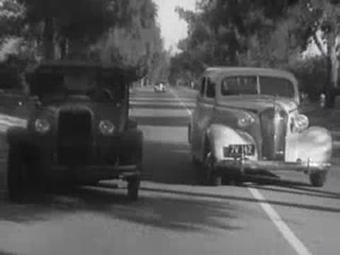 A vintage car passing another car on a tree-lined road.