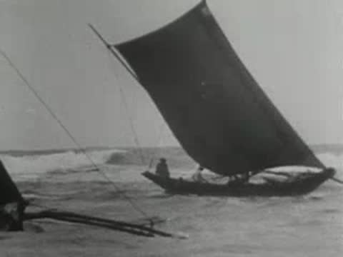 a small outrigger sailing boat moving through choppy ocean waves