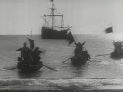 small rowing boats with people celebrating near the shore with a sailing ship behind
