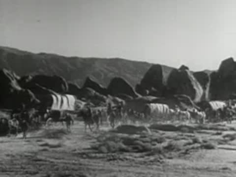 several horse-drawn covered wagons traveling through a rocky landscape with hills